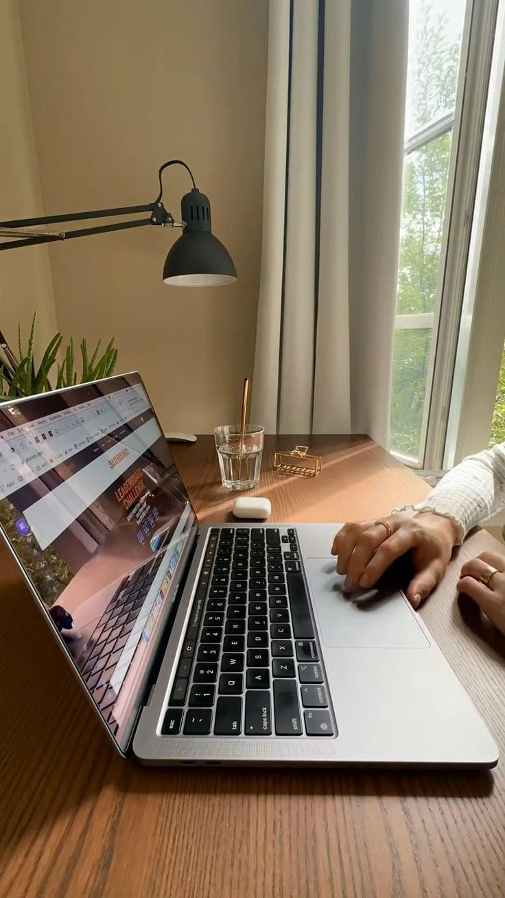 Mãos trabalhando em laptop sobre mesa de madeira junto à janela